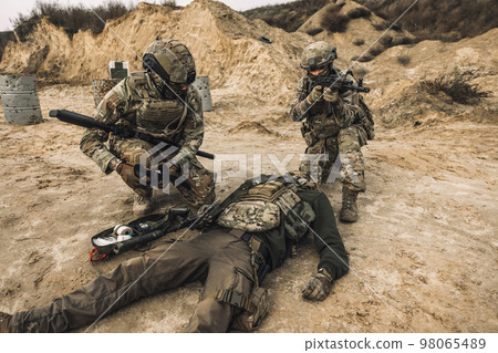 Soldiers near the wounded man examining him Soldiers near the wounded man examining him 98065489