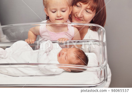 The sister and grandmother looks at a newborn baby in the hospital The sister and grandmother looks at a newborn baby in the hospital 98065537