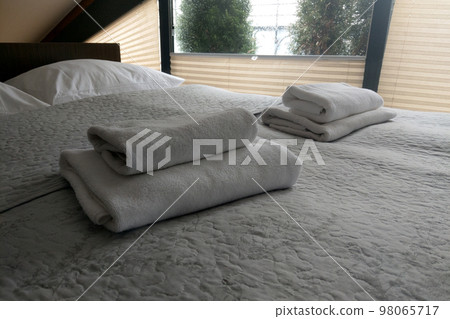 There are clean white towels on the bed. Hotel room. 98065717