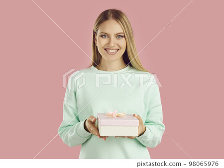 Beautiful satisfied woman holds small festive gift box in her hands on pink studio background. 98065976