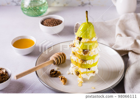Layers of pear, ricotta with walnut poured with honey on a plate on the table. Vitamin nutrition. 98066111
