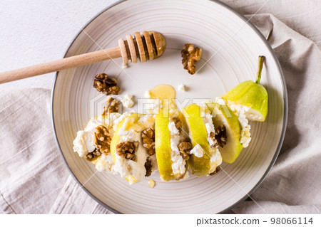 Pear with ricotta, honey and walnuts in layers on a plate. Healthy food. Top view. Closeup Pear with ricotta, honey and walnuts in layers on a plate. Healthy food. Top view. Closeup 98066114