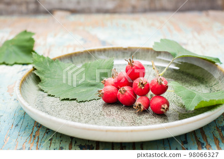 Hawthorn branch with berries and leaves on a plate on a rustic background Hawthorn branch with berries and leaves on a plate on a rustic background 98066327