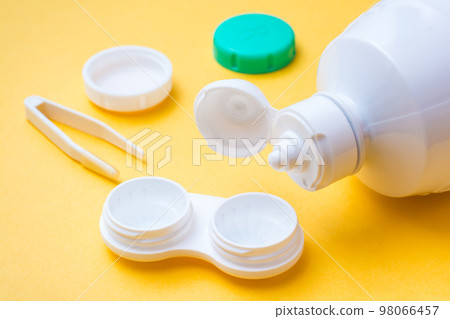 Contact lens cleaning fluid poured into an open container for storing lenses on a yellow background 98066457