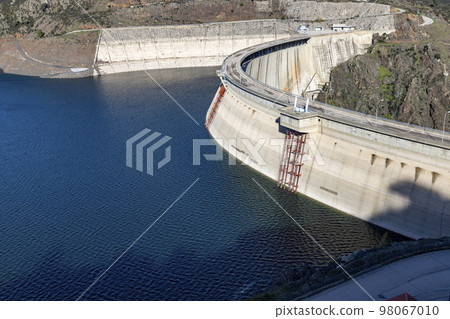 Reservoir. Prey. Dam located in the Atazar, north of the Community of Madrid. Damned water next to some green and pink mountains. Horizontal Photography Reservoir. Prey. Dam located in the Atazar, north of the Community of Madrid. Damned water next to some green and pink mountains. Horizontal Photography 98067010