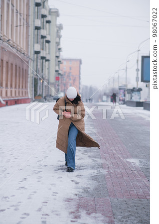 A girl in a long coat walks through the city in cold weather A girl in a long coat walks through the city in cold weather 98067022