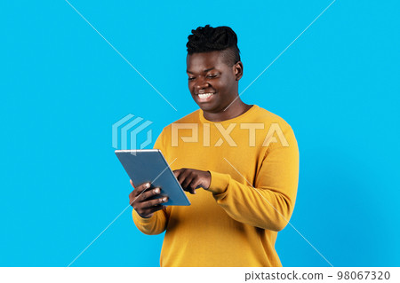 Smiling African American Male Using Digital Tablet While Standing Over Blue Background 98067320