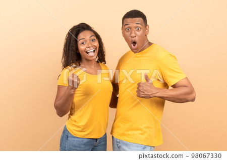 Joyful young african american couple celebrating success with thumb up and clenched fists, yellow background 98067330