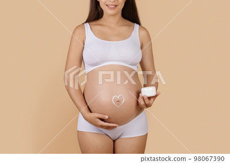 Pregnant woman with heart made of cream painted on her belly 98067390