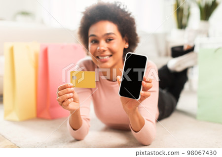 App for online shopping at home. Glad young mixed race lady shopaholic shows phone and credit card 98067430
