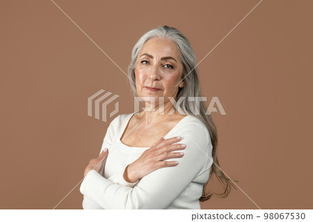 Serious pretty retired european female with gray hair looking at camera, isolated on brown background, studio Serious pretty retired european female with gray hair looking at camera, isolated on brown background, studio 98067530