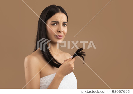 Unhappy brunette woman showing her dull long hair, beige background 98067695