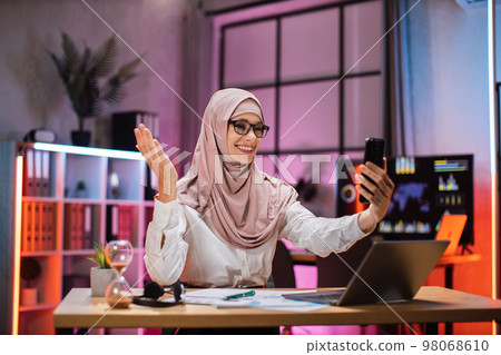 Portrait of smiling muslim businesswoman having mobile video conversation while sitting at table Portrait of smiling muslim businesswoman having mobile video conversation while sitting at table 98068610