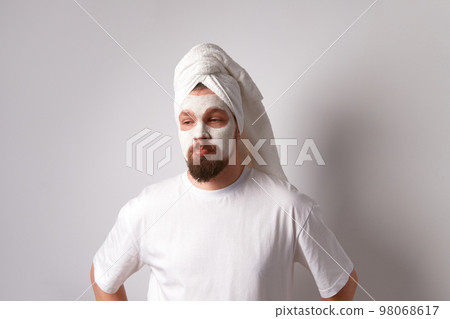 Man in white tshirt apply facial mask stand against white background. Beauty treatment, grooming and wellbeing concept Man in white tshirt apply facial mask stand against white background. Beauty treatment, grooming and wellbeing concept 98068617