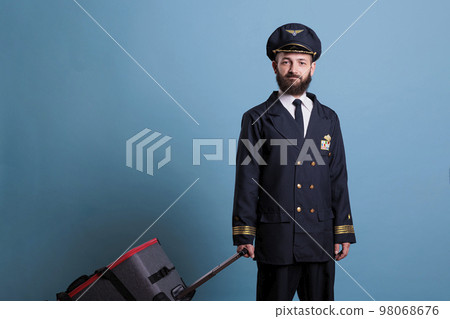 Airplane captain in professional airline uniform standing with suitcase, looking at camera. Ready pilot with luggage waiting for flight in airport, aviator holding baggage Airplane captain in professional airline uniform standing with suitcase, looking at camera. Ready pilot with luggage waiting for flight in airport, aviator holding baggage 98068676