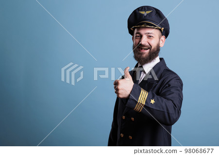 Smiling airplane pilot with thumb up gesture wearing professional uniform portrait, plane captain looking at camera. Aviator showing approval sign with finger, studio medium shot Smiling airplane pilot with thumb up gesture wearing professional uniform portrait, plane captain looking at camera. Aviator showing approval sign with finger, studio medium shot 98068677
