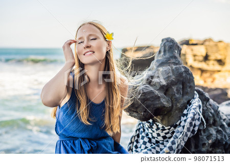 Woman is a tourist in Bali. The ritual of ablution with holy water and on her forehead prikleeli rice and put the flower ear Woman is a tourist in Bali. The ritual of ablution with holy water and on her forehead prikleeli rice and put the flower ear 98071513