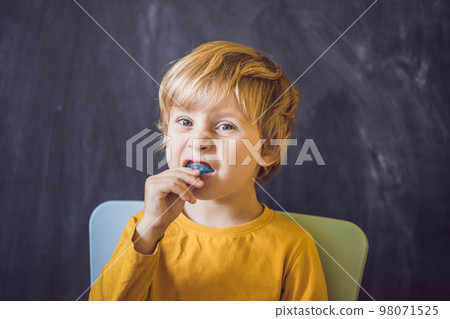 Three-year old boy shows myofunctional trainer. Helps equalize the growing teeth and correct bite, develop mouth breathing habit. Corrects the position of the tongue Three-year old boy shows myofunctional trainer. Helps equalize the growing teeth and correct bite, develop mouth breathing habit. Corrects the position of the tongue 98071525