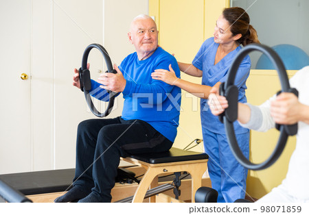 Elderly man exercising with pilates circle under supervision of female doctor 98071859