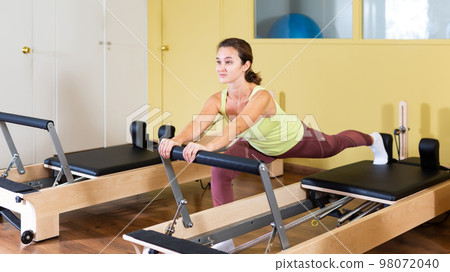 Young woman doing pilates exercises with reformer bed Young woman doing pilates exercises with reformer bed 98072040