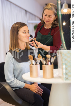 Elderly female makeup artist applying blush to woman face 98072491
