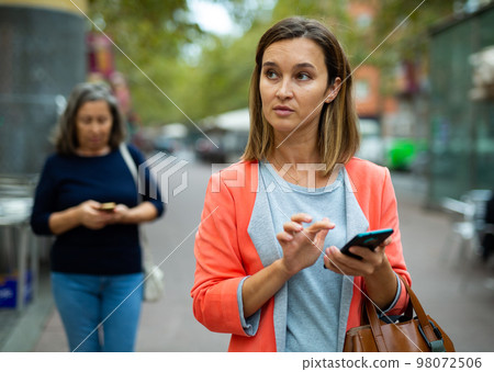 Focused young business woman using smartphone while walking outoors 98072506