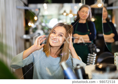 Young woman looking satisfied with hairdo in hairdressing salon 98072518