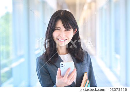 Young suit businesswoman looking at smartphone in office corridor 98073336