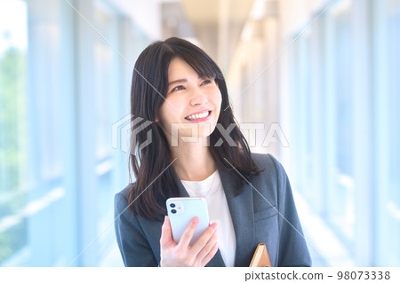Young suit businesswoman looking at smartphone in office corridor 98073338