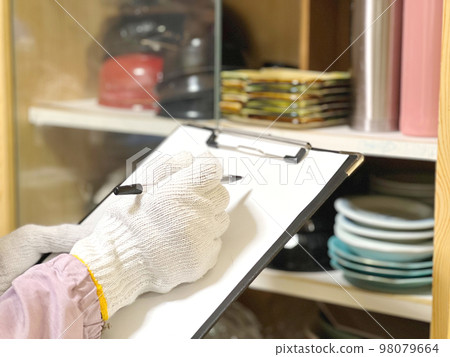 Gloved hand holding clipboard assessing cupboard Gloved hand holding clipboard assessing cupboard 98079664