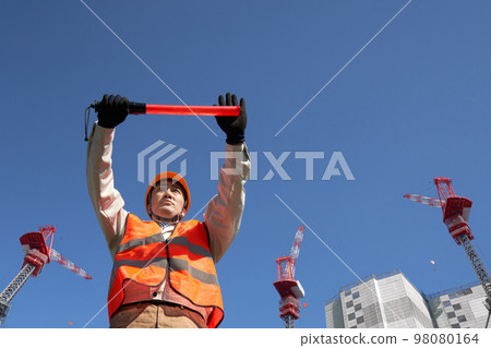 A man wearing a safety vest guiding traffic at a construction site 98080164