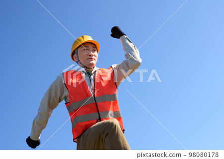 A man wearing a safety vest doing a guts pose under the blue sky A man wearing a safety vest doing a guts pose under the blue sky 98080178
