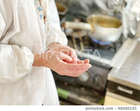 Elderly woman rubbing her hand in the kitchen Elderly woman rubbing her hand in the kitchen 98080285