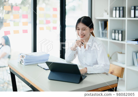 Portrait of a thoughtful Asian businesswoman looking at financial statements and making marketing plans using a computer on her desk. Portrait of a thoughtful Asian businesswoman looking at financial statements and making marketing plans using a computer on her desk. 98082005