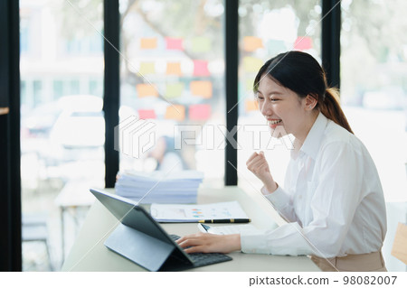Portrait of a woman business owner showing a happy smiling face as he has successfully invested her business using computers and financial budget documents at work. Portrait of a woman business owner showing a happy smiling face as he has successfully invested her business using computers and financial budget documents at work. 98082007