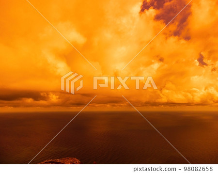 Aerial view red burning sunset over the sea with rocky volcanic cliff. Abstract nature summer sunset ocean sea background. Small waves on golden warm water surface Evening. Horizon. Nobody. No people. 98082658