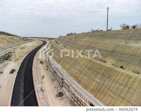 Mountain road constraction. Workers reinforce the slope over the new road. Road construction in progress on slope nature canyon. Infrastructure development and logistics. Aerial drone shot 98082674