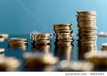 增加財富的形象。堆積在藍色背景上的硬幣和散景。 98084063