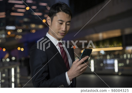 Businessman looking at the smartphone screen Building street at night 98084325