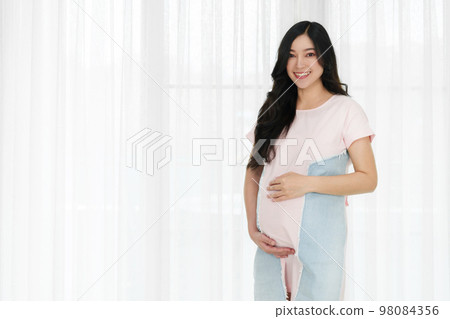 happy pregnant woman stroking belly on window background 98084356