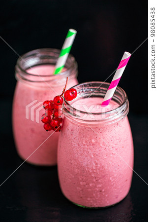 Side view of two jars with yogurt pink smoothie with berries on black background. Selective focus  98085438
