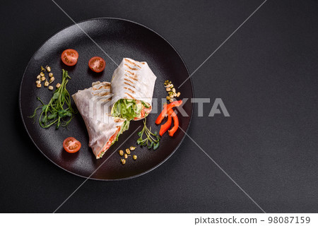Delicious fresh shawarma with tomatoes, peppers, cucumber on a dark concrete background Delicious fresh shawarma with tomatoes, peppers, cucumber on a dark concrete background 98087159