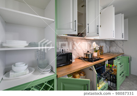 Doors open and drawers pulled out at new green and white kitchen furniture 98087331
