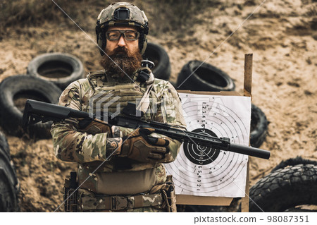 Mature soldier standing near the shooting target with rifle in hands Mature soldier standing near the shooting target with rifle in hands 98087351