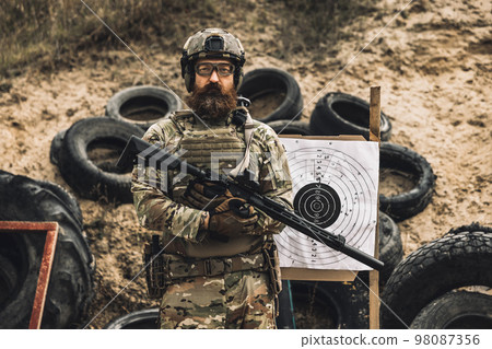 Mature soldier standing near the shooting target with rifle in hands Mature soldier standing near the shooting target with rifle in hands 98087356