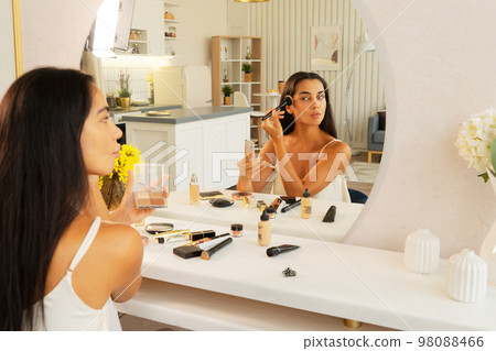 brunette woman with long straight dark hair and clean skin doing make up routine brunette woman with long straight dark hair and clean skin doing make up routine 98088466