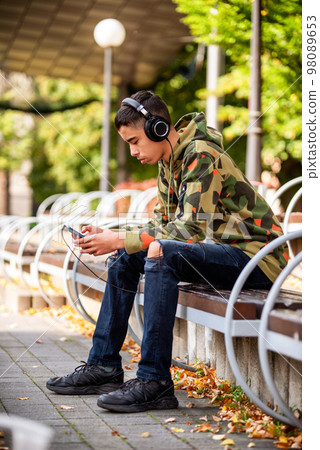 Young boy sitting on bench in park and listening music. 98089653
