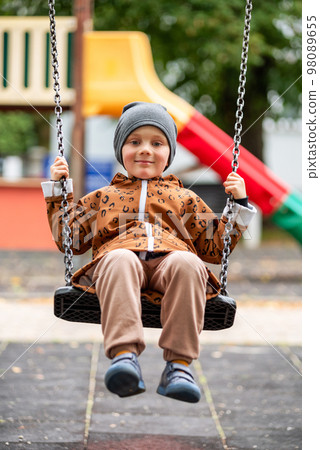 Happy boy swinging on a swing on playground Happy boy swinging on a swing on playground 98089655