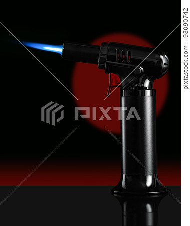 A gas blow torch kitchen with blue flame on the black background. A gas blow torch kitchen with blue flame on the black background. 98090742