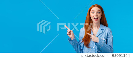 Overwhelmed amused pretty redhead teen girl in nightwear screaming excited and amazed, pointing upper left corner, drop jaw gasping astonished, cant resists temptation try new product 98091344